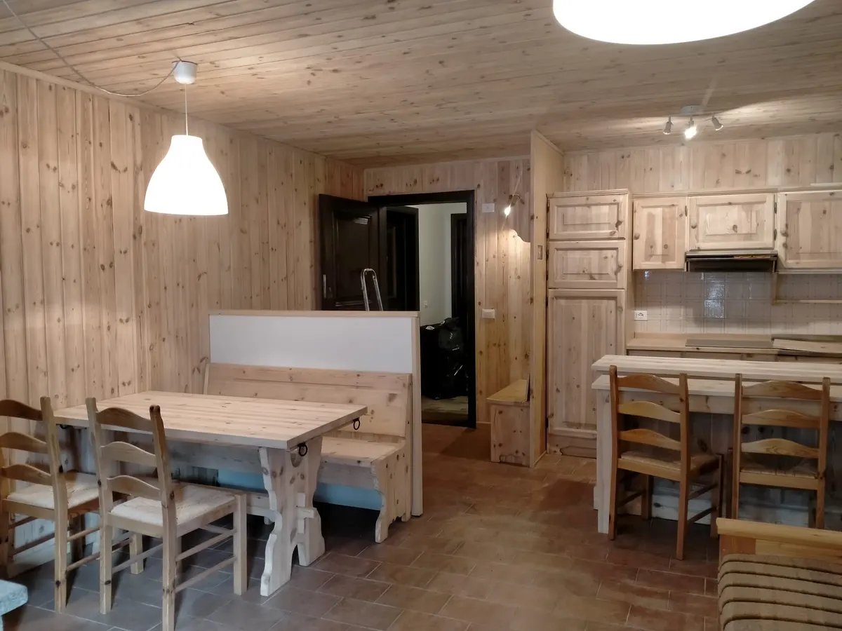 Cucina e soggiorno con soffitto in perline chiaro, tavolo rustico e panca