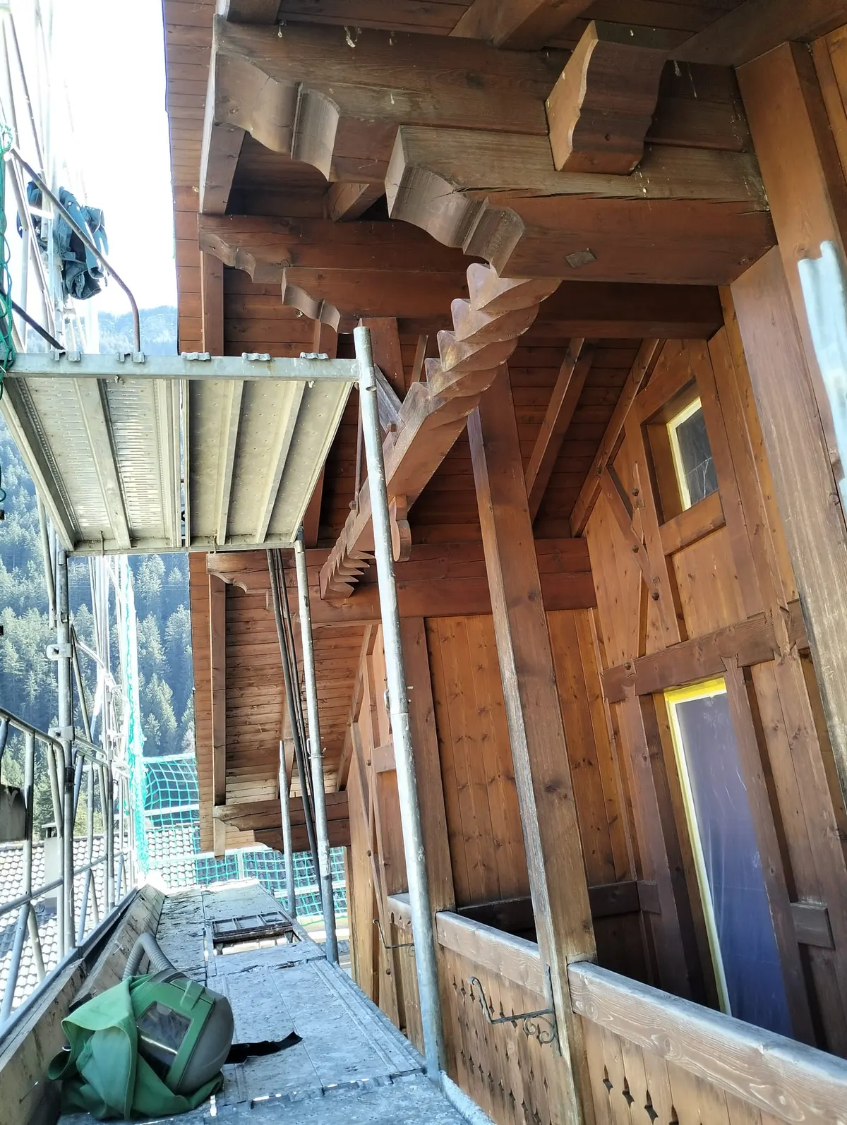 Fächerförmig geschnitzte Konsolen des Dachvorsprungs, noch dunkel, mit aufgestelltem Gerüst und abgedecktem Fenster
